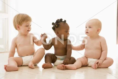 Three babies sitting indoors holding hands Stock Photos