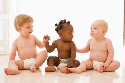 Three babies sitting indoors holding hands Stock Photos