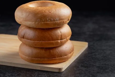 Three bagels stacked on top of each other on a wooden cutting board 写真素材