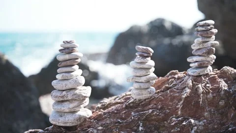 Three balanced pyramids of stones on the beach on the background of sea waves Stock Footage 134964747