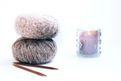 Three balls of delicate yarn, knitting needles and a candle on a bright backg Stock Photos