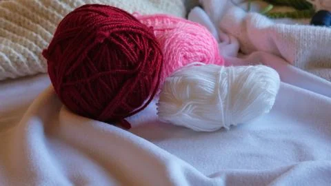 Three balls of wool yarn in red, pink and white are lying on a soft white fabric Stock-Fotos