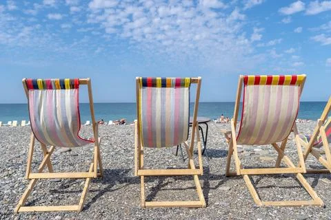 Three beach chairs are lined up on a beach, with the ocean in the backgroun. Stock Photos