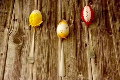 Three beautiful coloured Easter eggs laid on a table, each on one spoon Foto stock