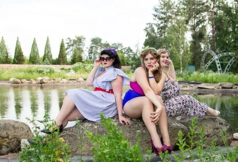 Three beautiful plus size models are sitting near the lake. Stock Photos