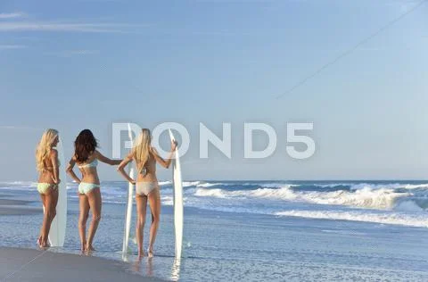 Three beautiful women surfers in bikinis with surfboards at beach Stock Photos
