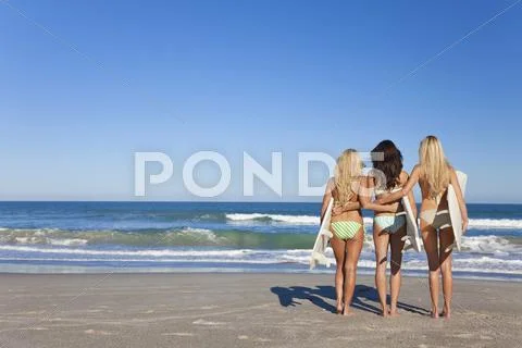 Three beautiful women surfers in bikinis with surfboards at beach Stock Photos