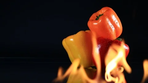 Three Bell Peppers with Out of Focus Fire in Foreground Roasting Over Black Stock Footage 104078227