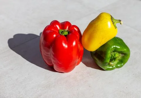 Three bell peppers on a white surface. Red, yellow, and green produce with Stock Photos