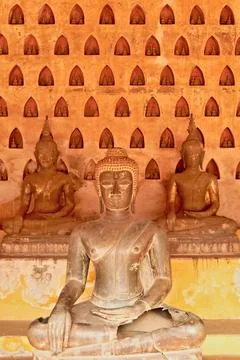 Three big buddha statues in front of a wall filled with many miniature buddha Foto stock