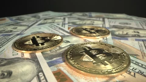 Three Bitcoins BTC are rotating on the table with 100 US dollars. Black Stock Footage 129831042