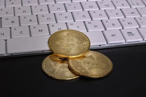 Three bitcoins on a computer keyboard closeup Stock Photos