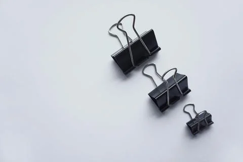 Three black binder clips of various sizes used to staple documents against Stock Photos