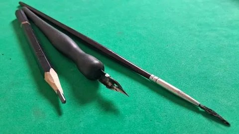 Three black drawing tools arranged neatly on a vibrant green surface Stock Photos