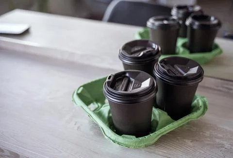 Three black plastic glasses with a drink stand on a light wooden table in the Stock Photos