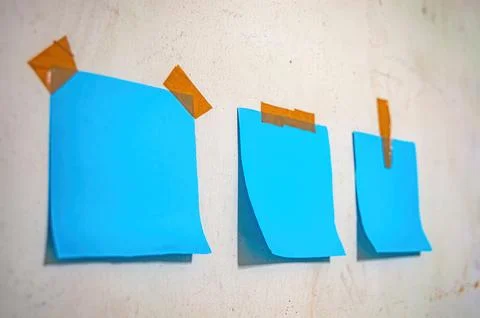 Three blank blue sticky notes taped to a light wall, ideal for themes of me.. Stock-Fotos