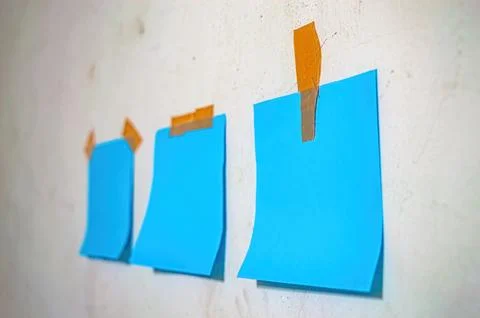 Three blank blue sticky notes taped to a textured white wall with orange ta.. Foto stock