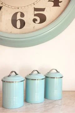 Three blank round kitchen containers and large wall clock on light background Stock Photos