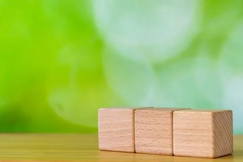 Three blank wooden cubes on table with blurred green nature bokeh  Stock-Fotos