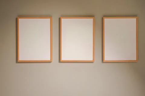 Three blank wooden frames hanging on a light gray wall creating an empty mo.. Stockfoto's