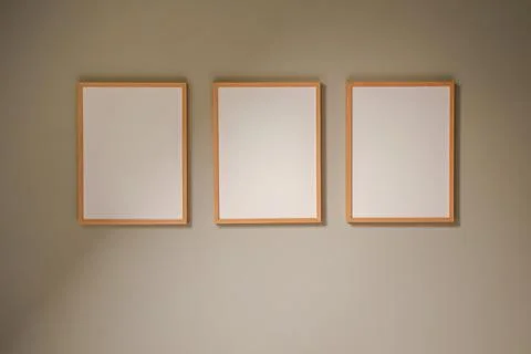 Three blank wooden frames hanging on a beige wall creating a triptych for a.. Fotos Stock