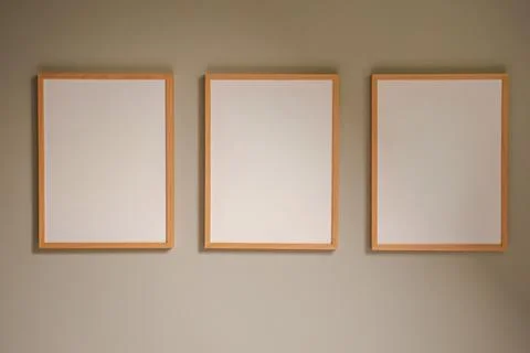 Three blank wooden frames hanging on a neutral wall creating a gallery layo.. Stock Photos
