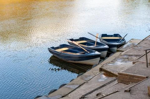 Three blue and white rowing boats moored on a tranquil river on a sunny day Stock Photos
