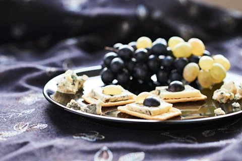 Three blue cheese crackers with grapes are on a black plate. Stock Photos