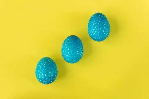 Three blue Easter eggs on bright yellow background, top view Stock Photos