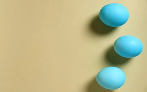 Three blue eggs on a beige background showing their smooth surface and round Stock Photos