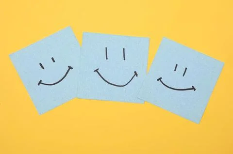 Three blue sticky notes with happy smiley faces on yellow background Stock Photos