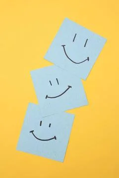 Three blue sticky notes with happy smiley faces on yellow background Stock Photos