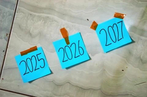Three blue sticky notes labeled 2025, 2026, and 2027 taped to tile floor wi.. Stock-Fotos