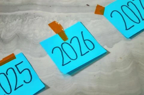 Three blue sticky notes labeled 2025, 2026, and 2027 taped to white marble .. 스톡 사진