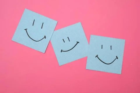 Three blue sticky notes with smiley faces on pink background Stock Photos