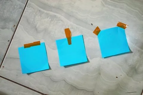 Three blue sticky notes taped to tiled floor in a row, each with a differen.. Fotos Stock