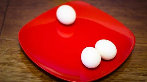 Three boiled chicken eggs stand on a square plate in red Stock Photos