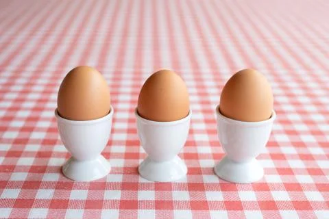 Three boiled eggs in egg cups in a row on a table Stock Photos