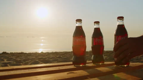 Three bottles Coca Cola sandy beach at sunrise. man hand takes bottle of cola Stock Footage 200490485