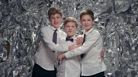 Three Boys On Shiny Background. New Year Celebration. Two Older Boys Hug Smaller Stock Footage 180361296