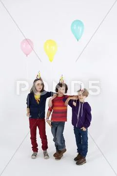 Three boys wearing party hats and holding balloons, in a row Stock Photos
