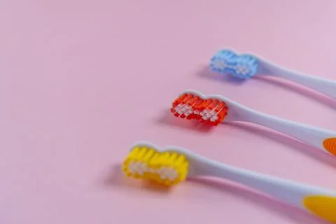 Three bright toothbrushes on a delicate pink background. Red, yellow, blue 스톡 사진