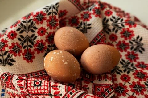 Three brown chicken eggs with white speckles resting on a traditional fabric 库存照片