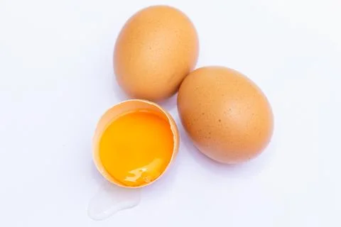 Three brown eggs With one egg broken in half, with a yolk inside the eggshell Stock Photos