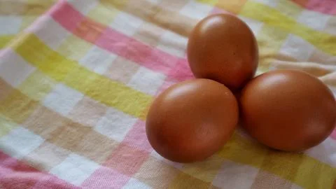 Three brown eggs on pastel checkered cloth with copy space Stock Photos
