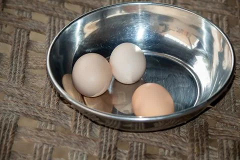 Three Brown Eggs in a Stainless-Steel Bowl on Woven Surface Stock-Fotos