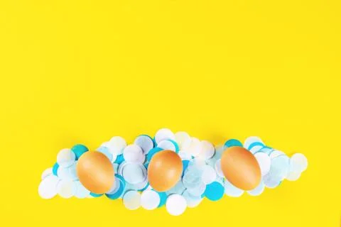 Three brown eggs on yellow background with confetti. Stock Photos