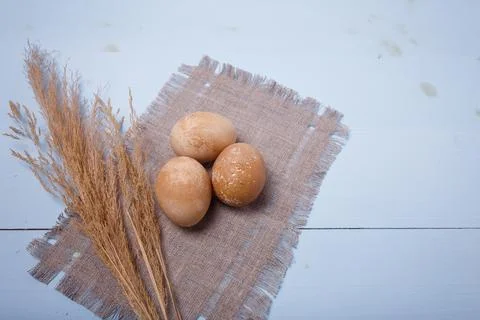 Three brown painted Easter eggs on sack mat with dry branches on blue wooden Stock Photos