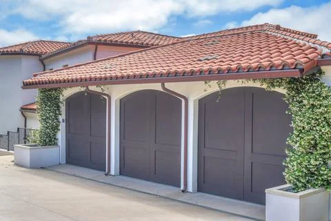 Three brown side-hinged garage doors and two concrete planters with vines Stock Photos