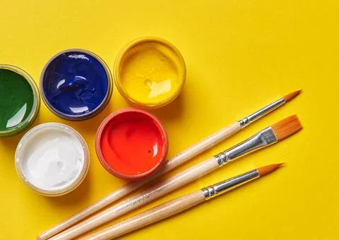 Three brushes and bright cans of paint on a yellow background Stock Photos
